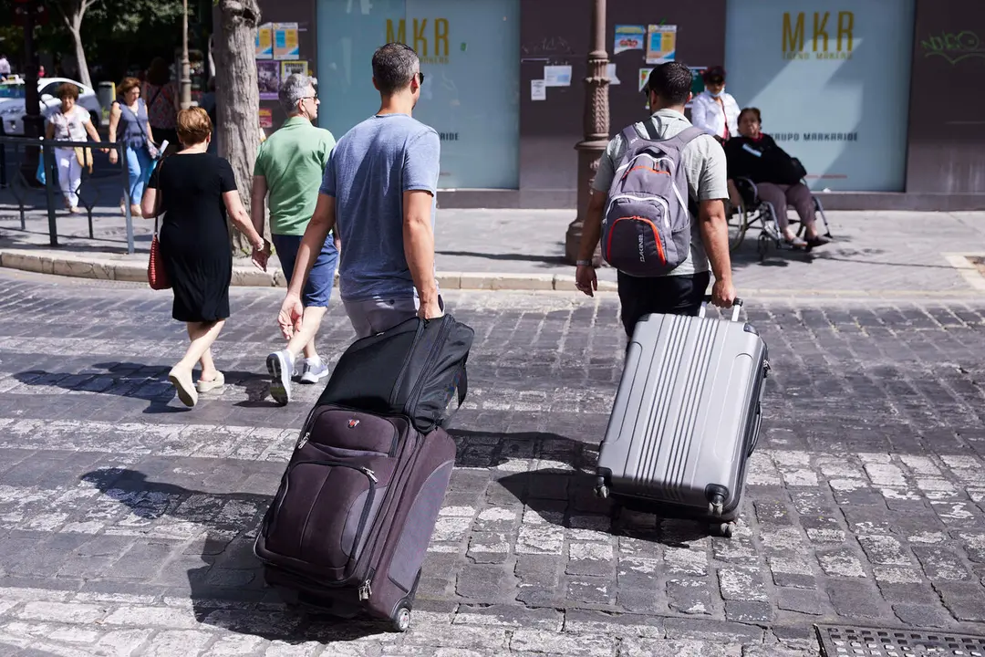  Dos turistas, con maletas, cruzan un paso de peatones en Sevilla. | Archivo 